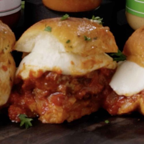 Garlic parmesan meatball sliders with melted cheese on slider buns, garnished with fresh herbs on a dark serving board