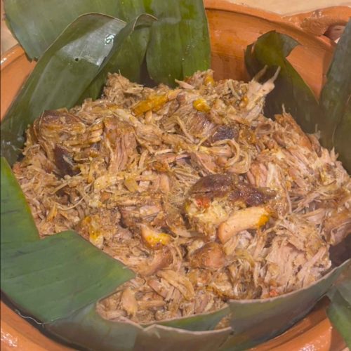 Shredded cochinita pibil served in large green banana leaves with visible chunks of meat and aromatic spices