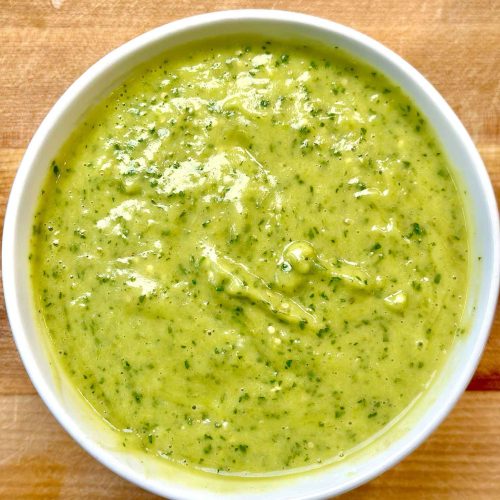 Bowl of green jalapeño avocado salsa with visible herbs and chunky texture on wooden surface