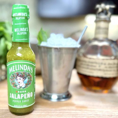 Melinda's Jalapeño Pepper Sauce bottle next to cocktail shaker and whiskey bottle for making spicy mint julep