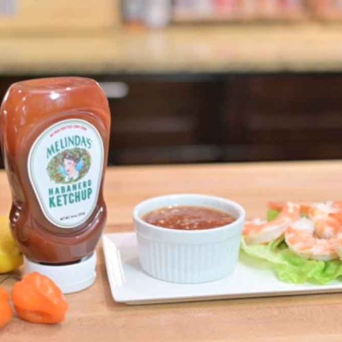 Melinda's Habanero Ketchup bottle next to shrimp cocktail with spicy dipping sauce in white bowl on wooden surface