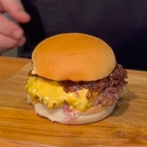 Cheesy chipotle bacon jam burger with melted yellow cheese and crispy bacon on a brioche bun, placed on a wooden board