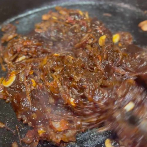 Caramelized bacon chipotle jam cooking in a stainless steel pan with golden brown onions and spices