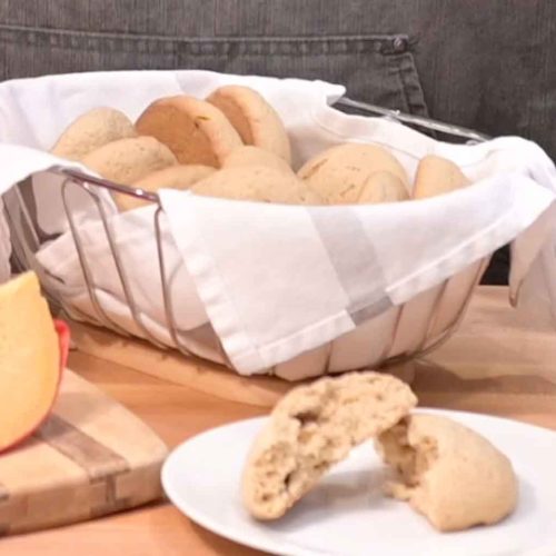 Fresh baked Belizean powder buns in wire basket lined with white cloth, with broken bun showing texture on plate