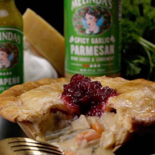 Thanksgiving pot pie with cranberry sauce on top and flaky golden crust, with Melinda's hot sauce bottles in background