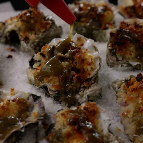 Baked oysters topped with green herbs and breadcrumbs on ice with red cocktail picks
