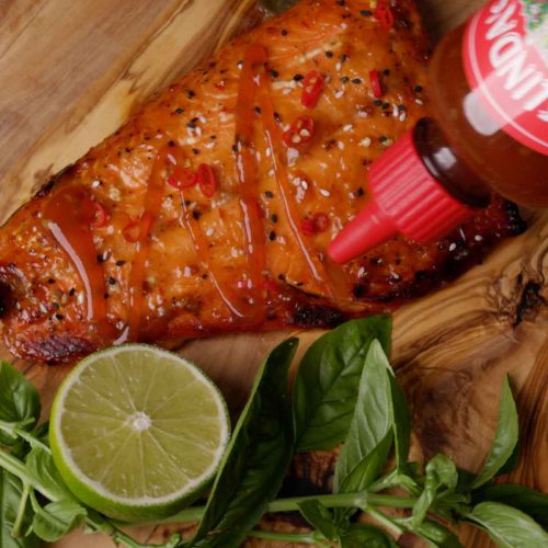 Glazed salmon fillet on wooden board with lime half and fresh basil leaves, seasoned with black pepper