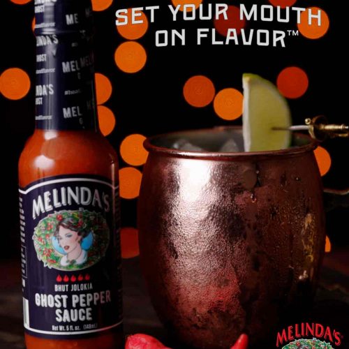 Copper mug containing Melinda's Ghost Moscow Mule cocktail with lime garnish next to bottle of Melinda's Ghost Pepper Sauce