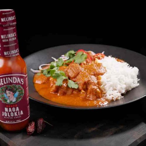 Spicy chicken madras curry with white rice on a dark plate, garnished with cilantro, alongside Melinda's Naga Jolokia hot...