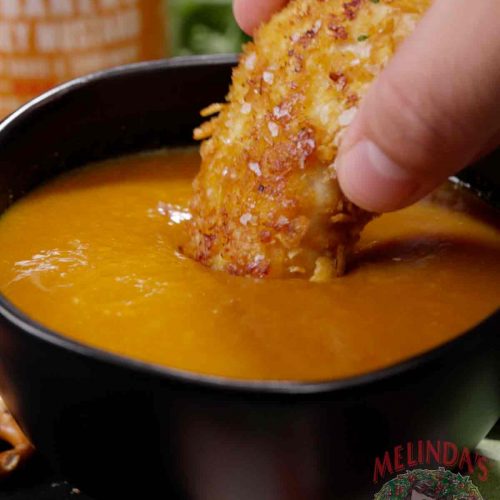Hand dipping a crispy golden appetizer into a bowl of orange maple habanero honey mustard sauce