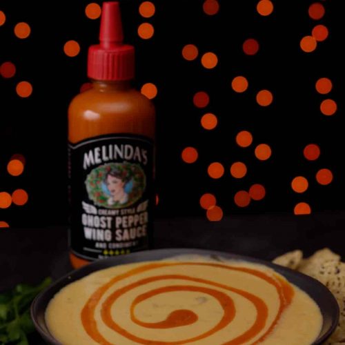 Melinda's Ghost Pepper Wing Sauce bottle next to a bowl of creamy queso with orange sauce swirled on top