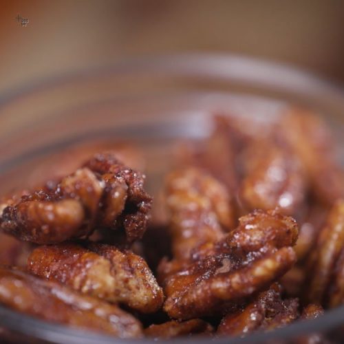 Glossy candied pecans with red chili coating in a wooden bowl, glistening with sweet and spicy glaze