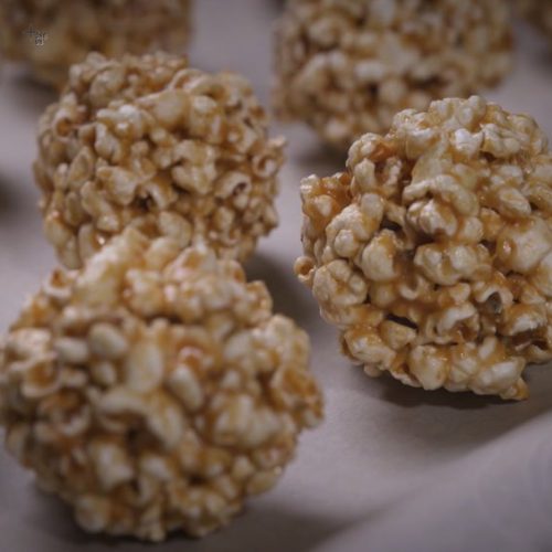 Golden caramel popcorn balls with visible kernels clustered together on a white surface