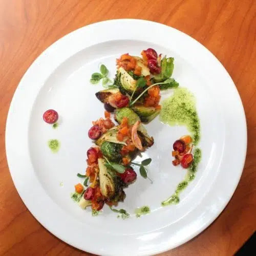 Elegant plated Brussels sprouts dish with cranberries, herbs, and green sauce drizzle on white plate