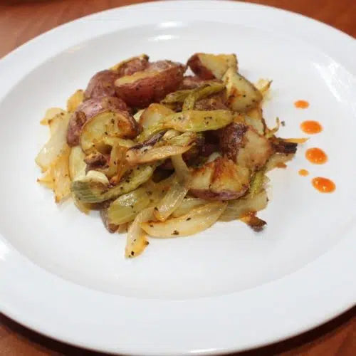 Roasted red potatoes with caramelized onions and herbs on a white plate, garnished with orange sauce dots
