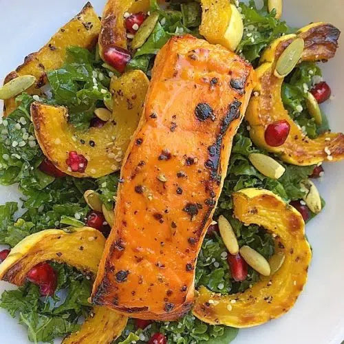 Grilled salmon fillet with scotch bonnet pepper seasoning on bed of mixed greens with roasted squash and pomegranate seeds