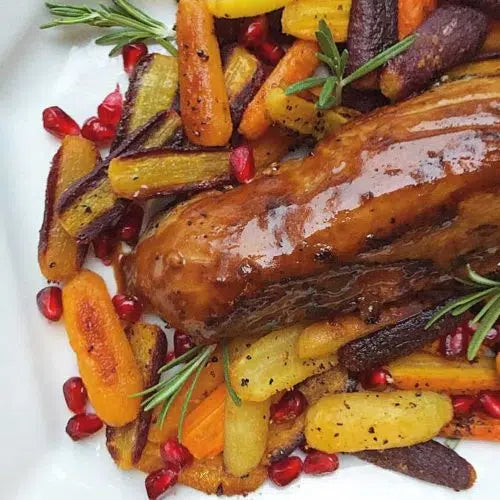Glazed pork tenderloin with roasted rainbow carrots, fresh rosemary, and pomegranate seeds on a white plate