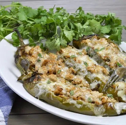 Roasted green Hatch chiles stuffed with filling and topped with melted cheese, garnished with fresh cilantro on white plate