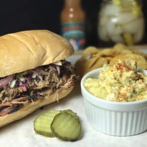 Cochon de lait sandwich with pulled pork and purple cabbage, served with potato salad and pickle slices