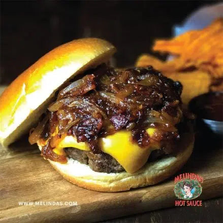 Juicy burger with melted cheddar cheese and caramelized onions on a bun, served with sweet potato fries on a wooden board.