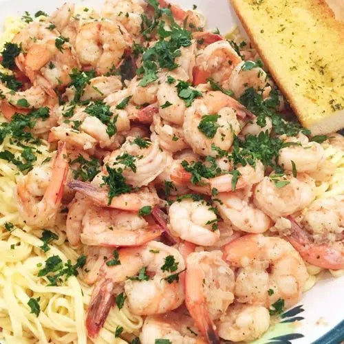 Garlic shrimp scampi with parsley served over pasta alongside buttered garlic bread