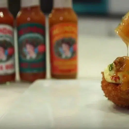 Chicken fried deviled eggs with hot sauce bottles in background on white surface