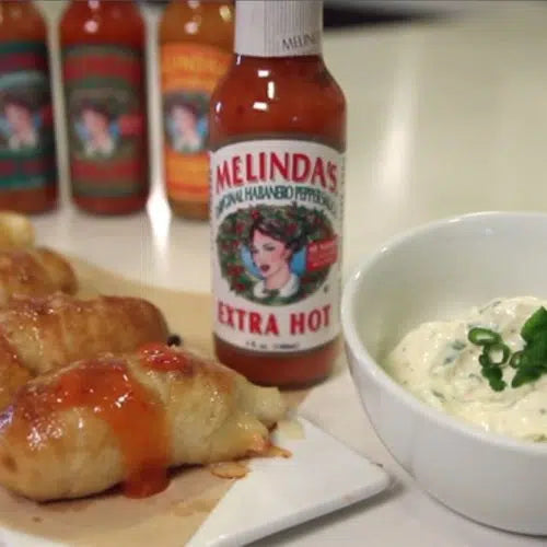 Stuffed pretzel bites with hot sauce drizzle next to Melinda's Extra Hot sauce bottle and bowl of white dipping sauce
