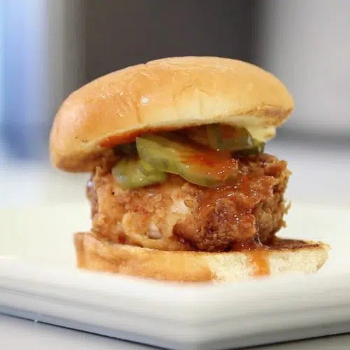Golden fried chicken sandwich with pickles and sauce on a brioche bun, served on a white plate