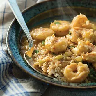 Bowl of shrimp etouffee with rice, featuring plump shrimp in a rich brown roux-based sauce, served in a dark ceramic bowl