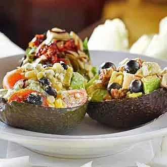 Two halved avocados filled with colorful vegetable salad including tomatoes, olives, and cheese on a white plate