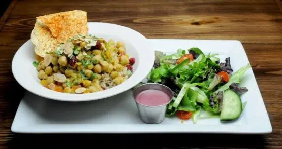 White plate with chickpea curry, cornbread slice, and side salad with pink dressing on wooden table