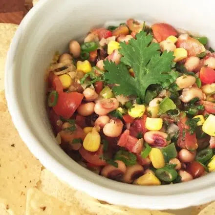 Colorful black-eyed pea salsa with tomatoes, corn, herbs and beans in white bowl, served with tortilla chips
