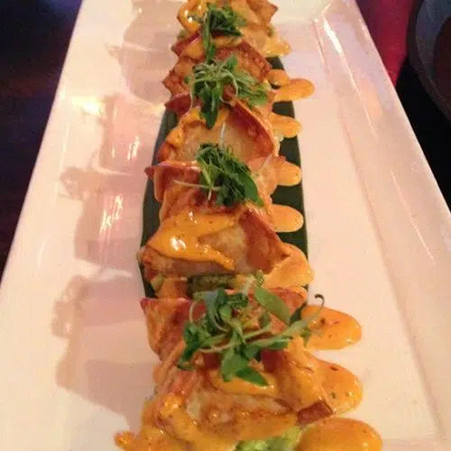 Plated tinga de pollo wontons topped with orange sauce and fresh green herbs on white rectangular serving dish