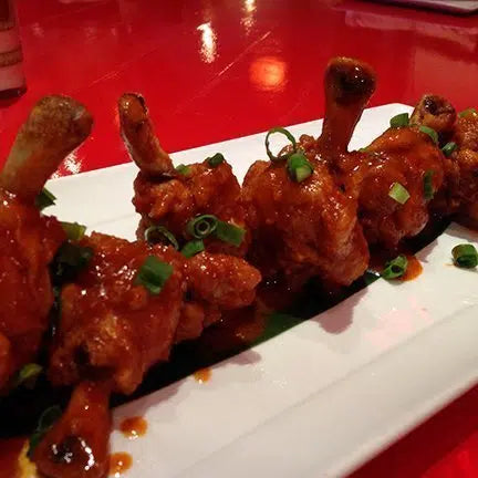Glazed chicken wings with spicy sauce garnished with chopped green onions on white rectangular plate
