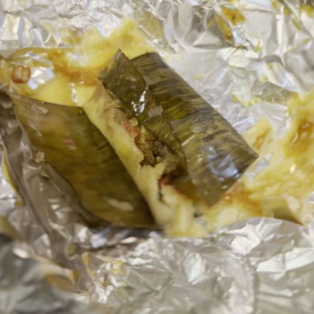 Unwrapped Belizean chicken tamale with banana leaf wrapping and melted cheese on aluminum foil