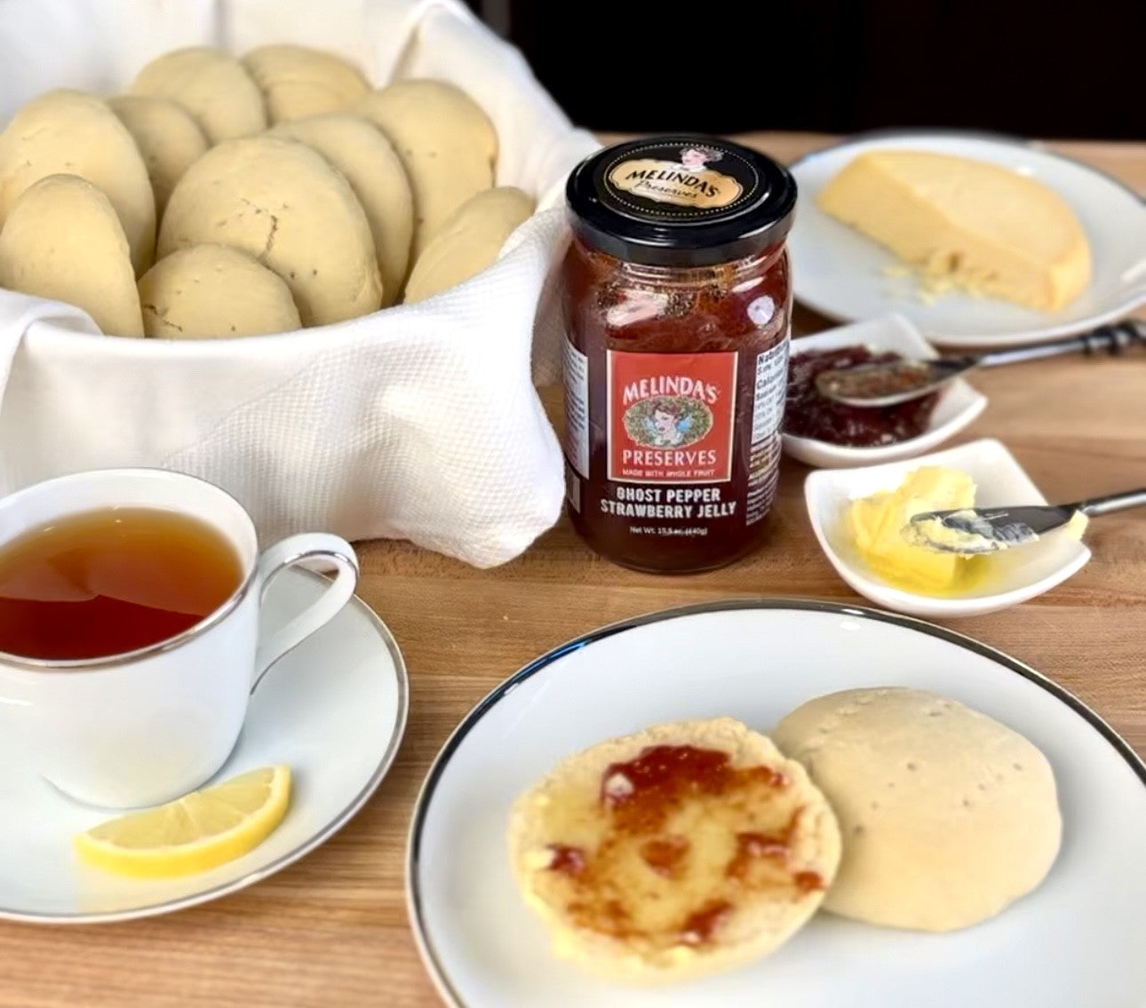 Johnny cakes on plate with Melinda's Ghost Pepper Strawberry Jelly, tea cup, butter, and bag of potatoes on wooden table