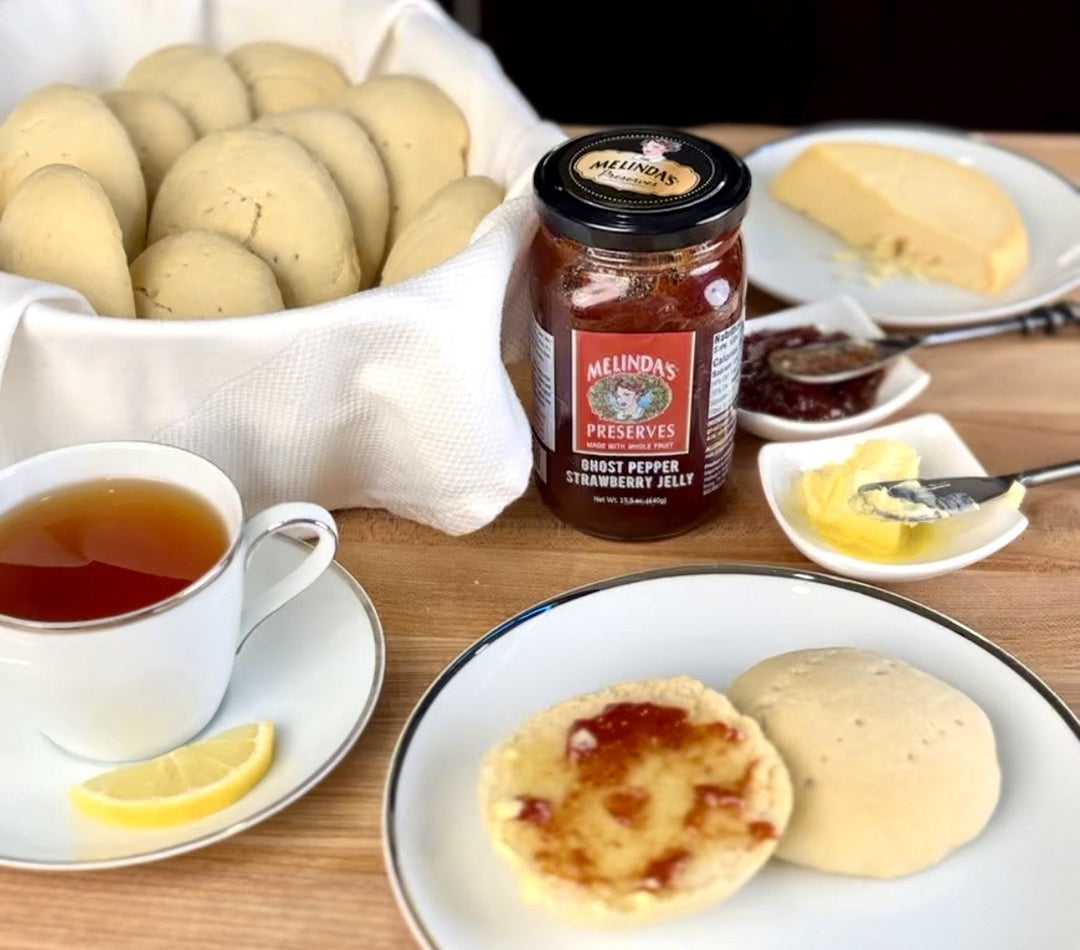 Johnny cakes on plate with Melinda's Ghost Pepper Strawberry Jelly, tea cup, butter, and bag of potatoes on wooden table
