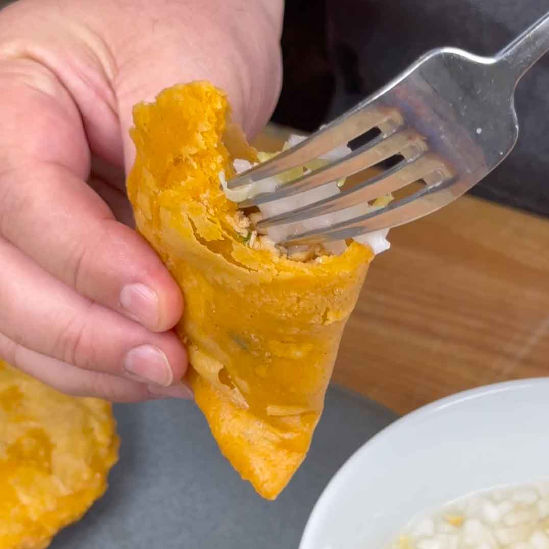 Hand using fork to eat golden-yellow Belizean panade, showing flaky pastry texture and filling
