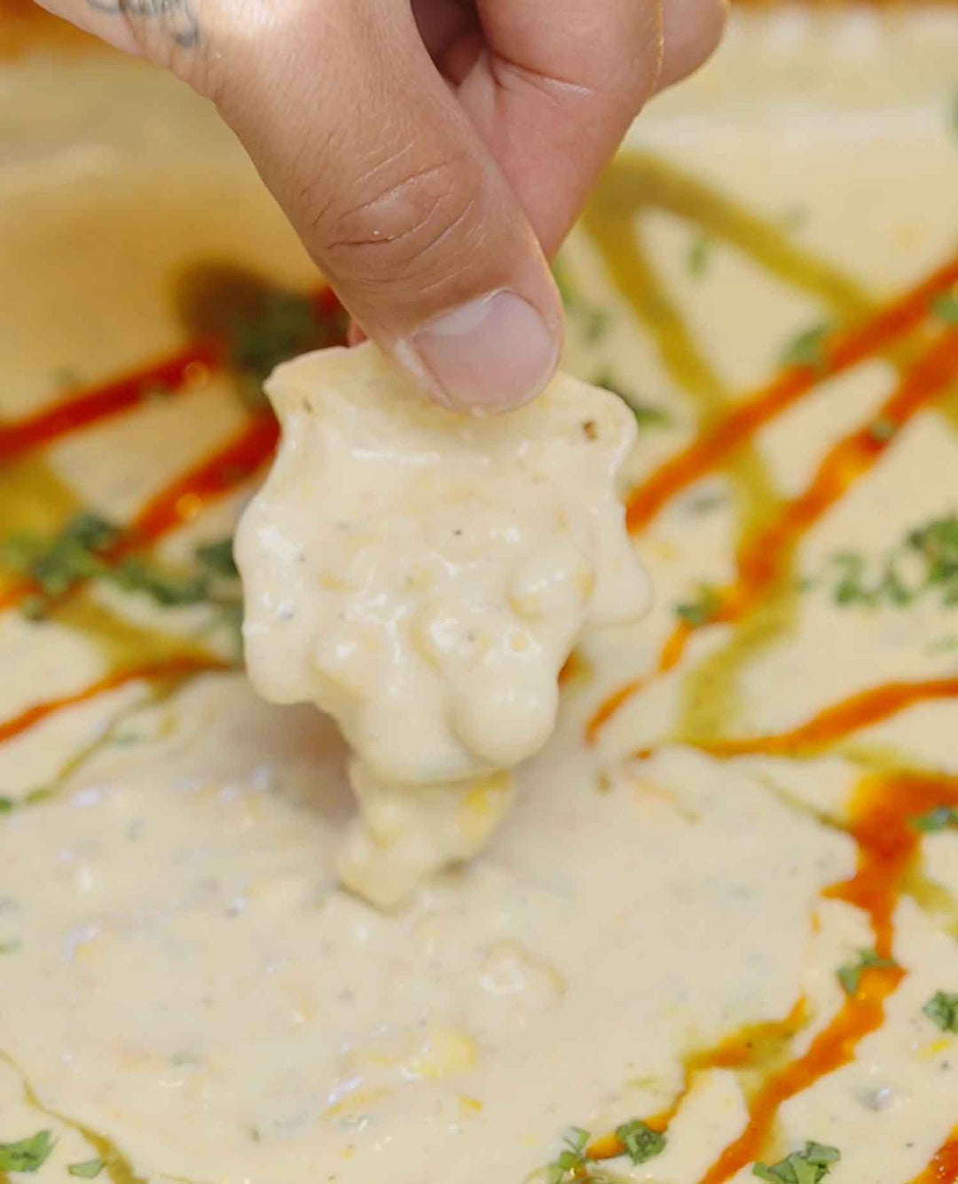 Hand holding a tortilla chip with creamy corn dip, with colorful chips scattered in background