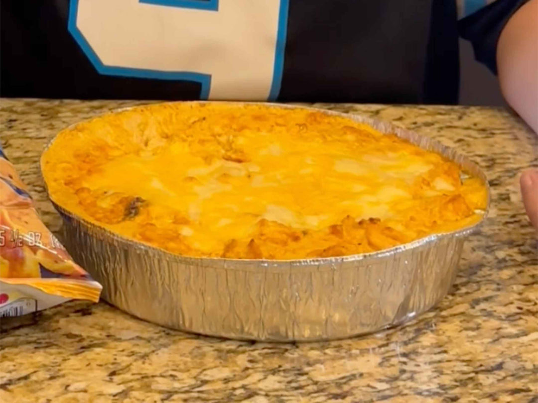 Golden buffalo chicken dip with melted cheese top in aluminum pan on granite counter