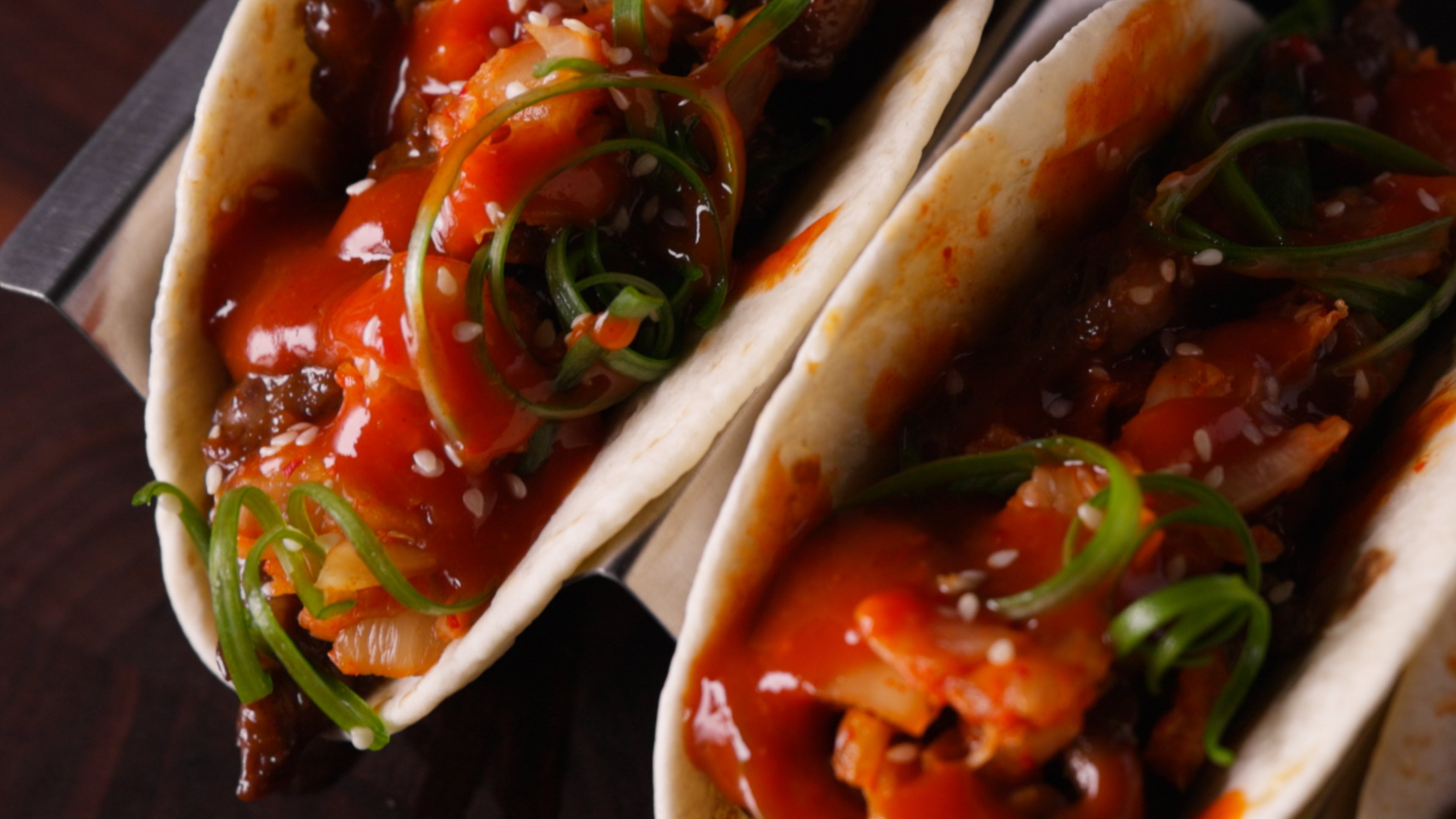 Two Korean-style tacos filled with glazed meat, bell peppers, and green onions on soft flour tortillas