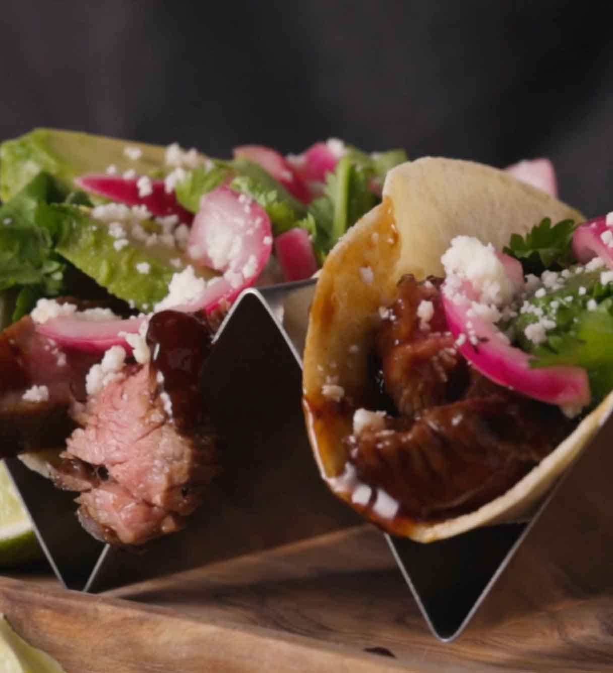 Glazed steak tacos topped with pickled red onions, white cheese crumbles, and fresh cilantro served in metal holders