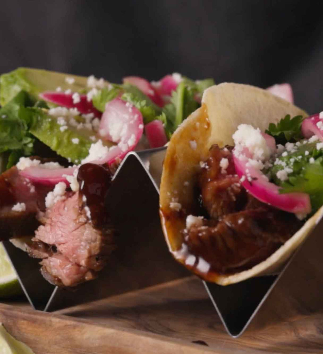Glazed steak tacos topped with pickled red onions, white cheese crumbles, and fresh cilantro served in metal holders