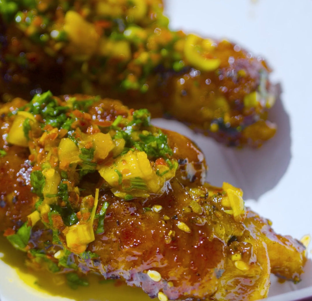 Glazed chicken wings topped with diced green herbs and yellow garnish on a white plate