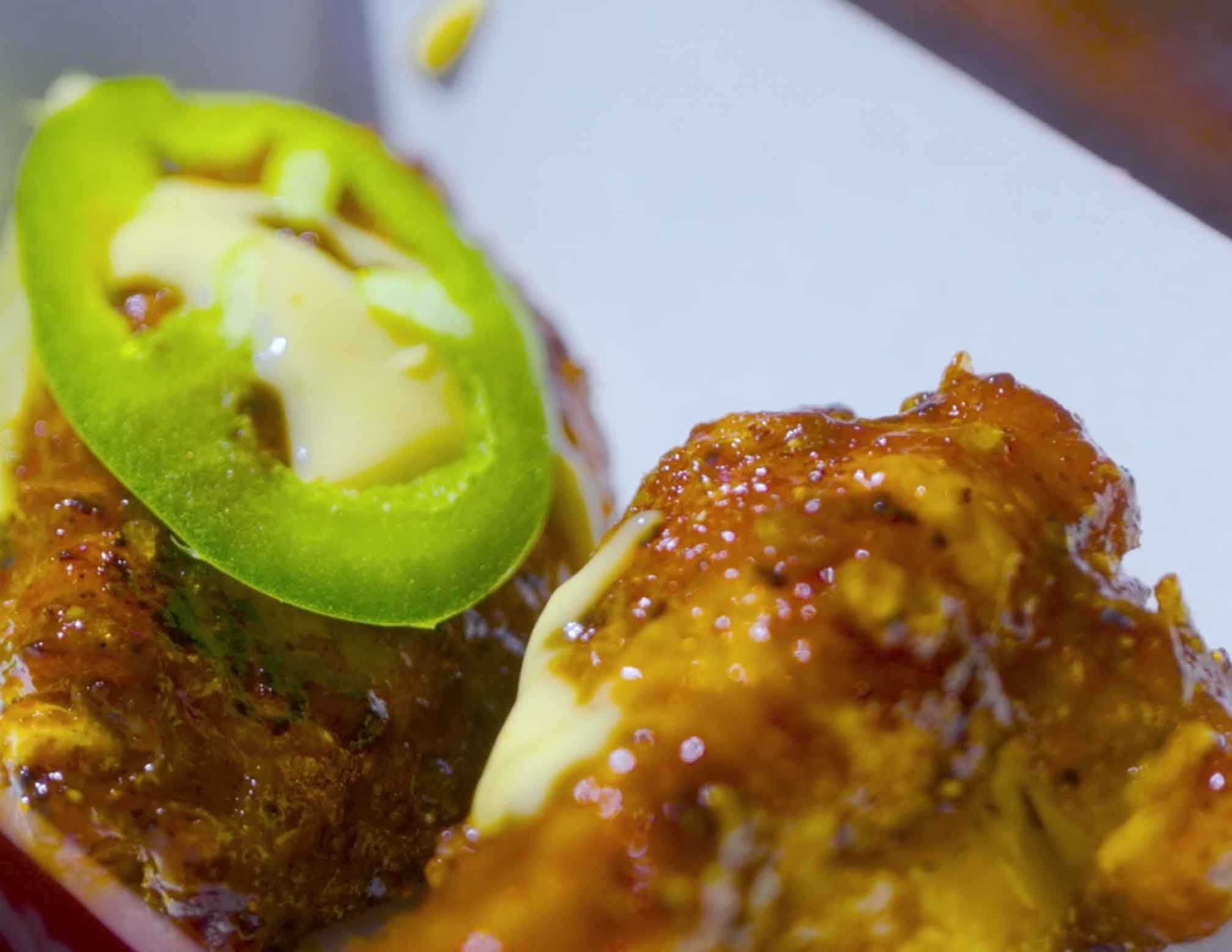 Glazed chicken wings topped with sliced jalapeños on a white plate, featuring golden-brown caramelized coating