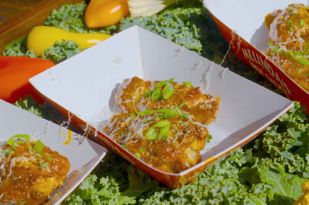 Golden glazed chicken wings in takeout containers garnished with green onions, surrounded by fresh kale and bell peppers