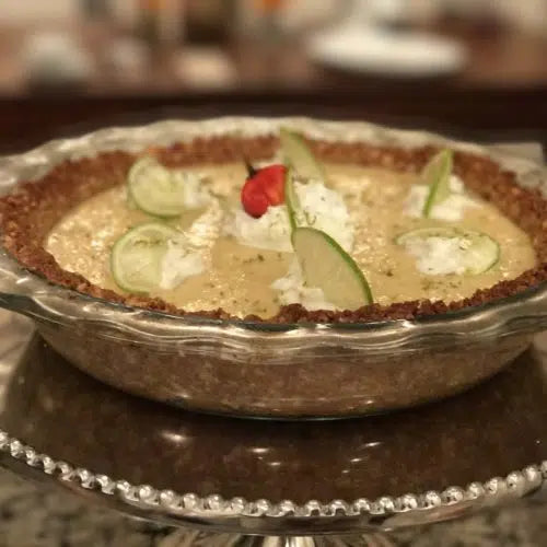 Mango habanero key lime pie in glass dish topped with lime slices and red pepper garnish on decorative plate