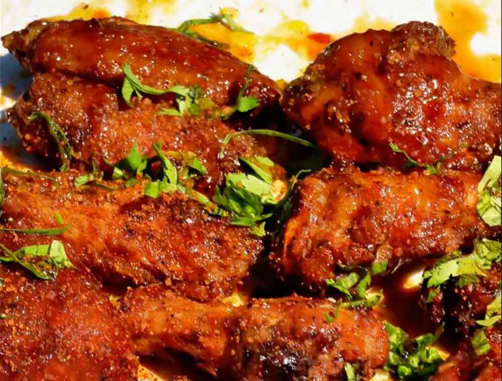 Glossy glazed chicken wings garnished with fresh green herbs, featuring a rich reddish-brown sauce coating