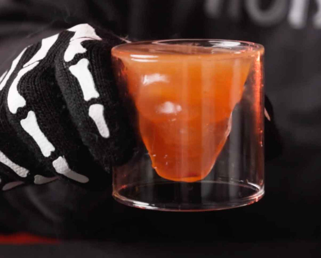 Orange layered cocktail in clear glass next to black and white patterned cloth napkin on dark surface