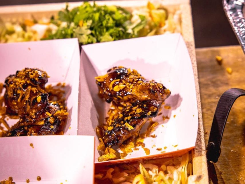 Glazed chicken wings with golden sauce in white paper containers, served with salad in background